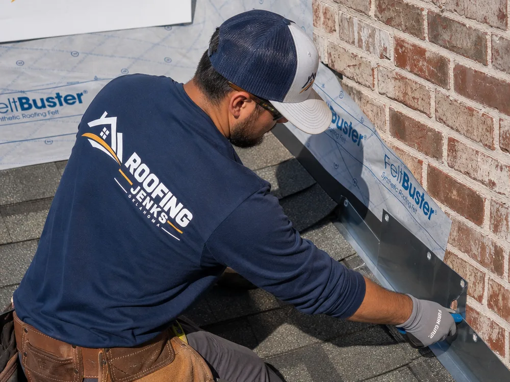 Roofer installing step flashing and underlayment at a roof-to-wall intersection